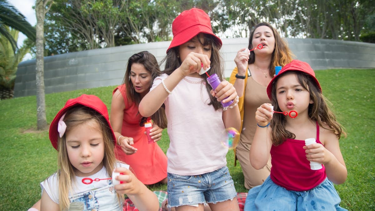 Happy children and adults enjoying bubble-blowing in a sunny park, creating joyful summer memories.