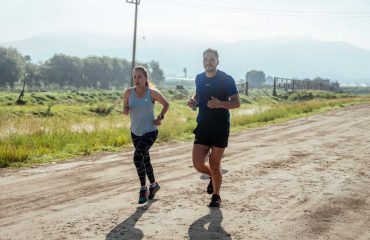 Active couple jogging on a dirt road in a scenic rural area under the bright sun.